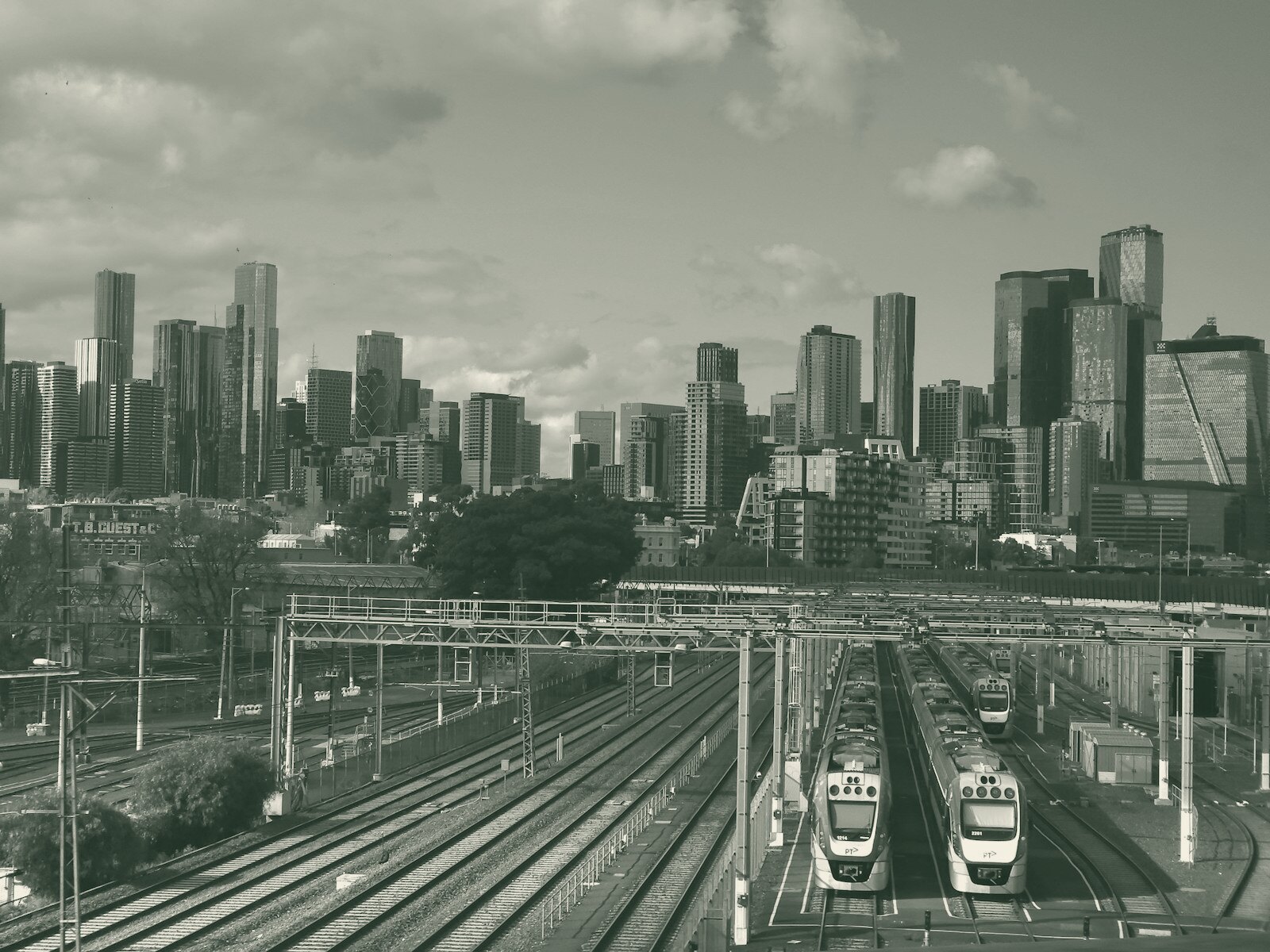 A train station with two trains on the tracks and a city in the background