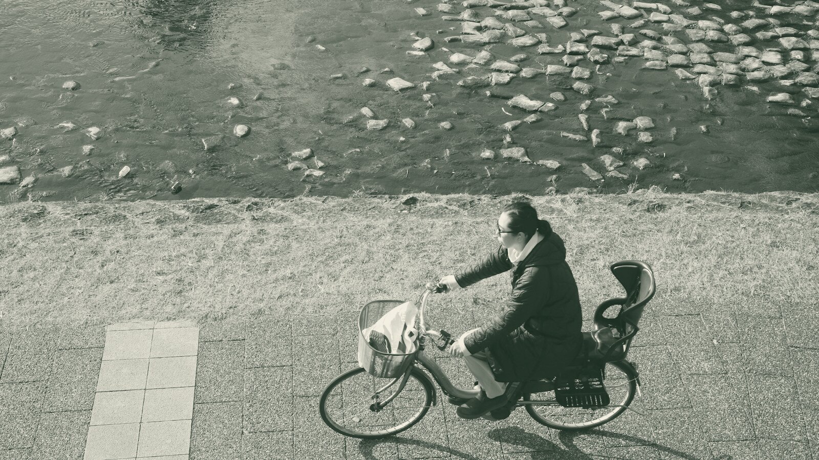 Person riding a bicycle with child seat near water