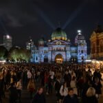 Crowds gather at Federation Square under colorful light projections during Melbourne’s Winter Festival 2025, with Flinders Street Station in the background.