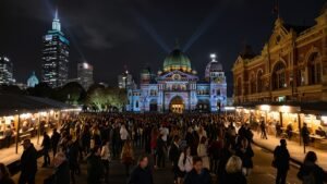 Crowds gather at Federation Square under colorful light projections during Melbourne’s Winter Festival 2025, with Flinders Street Station in the background.